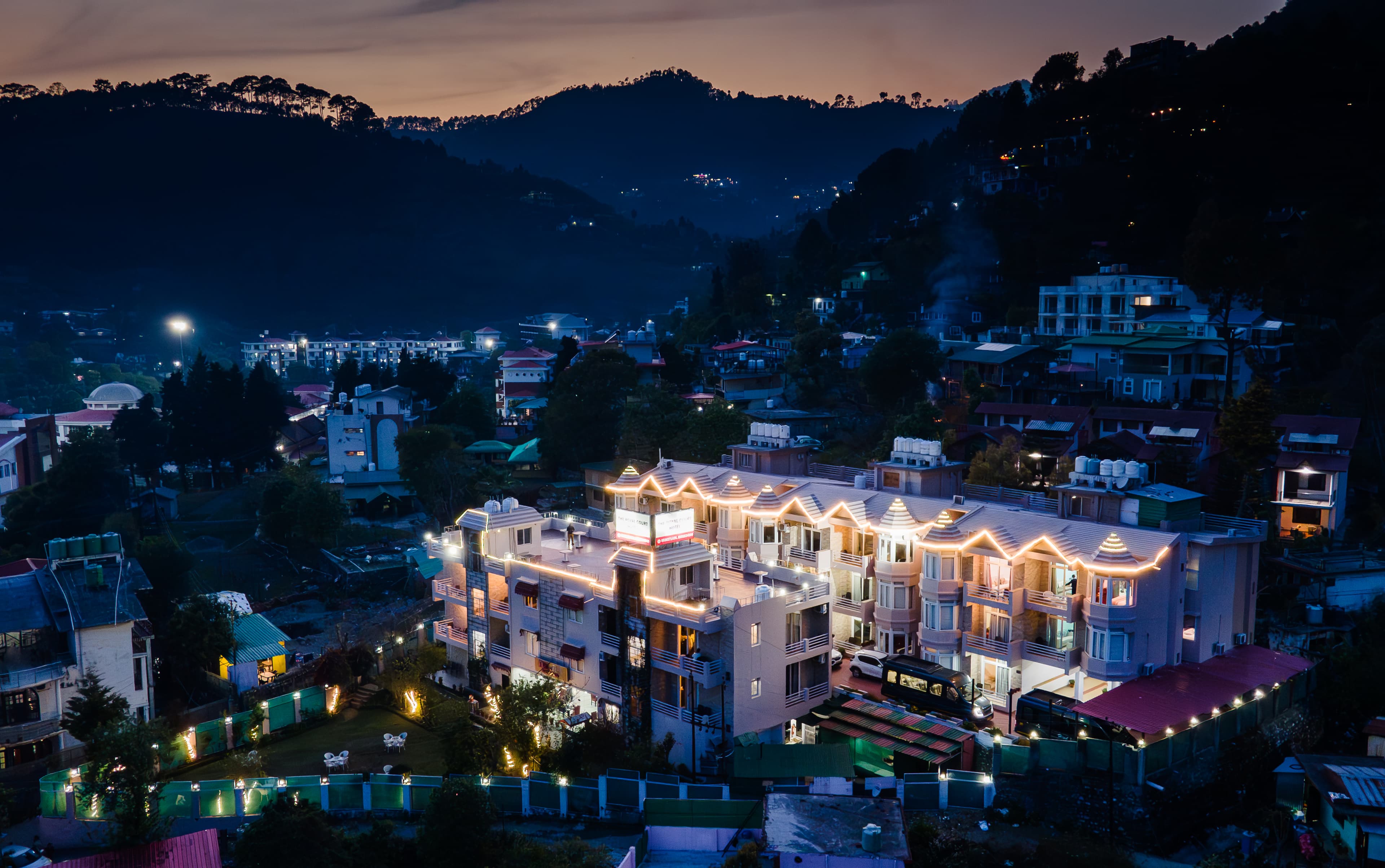 Aerial evening view of The Royal Court by Vikalp illuminated against the Bhimtal hills